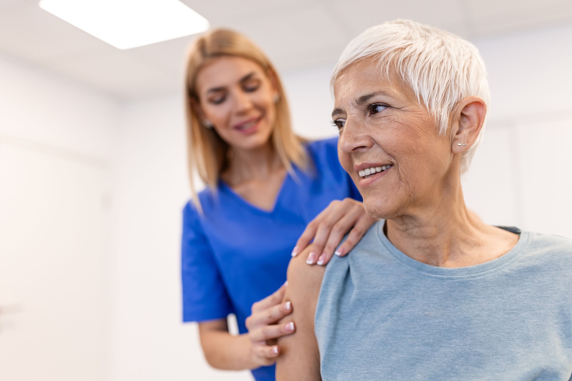 Woman doctor osteopath in medical uniform fixing senior woman patients shoulder and back joints in manual therapy clinic during visit. Professional osteopath during work with patient concept